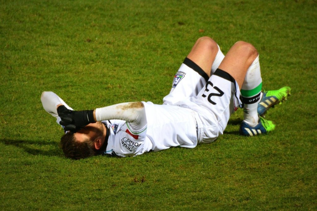 サッカーフィールドで怪我して倒れ込むボロボロの男性
